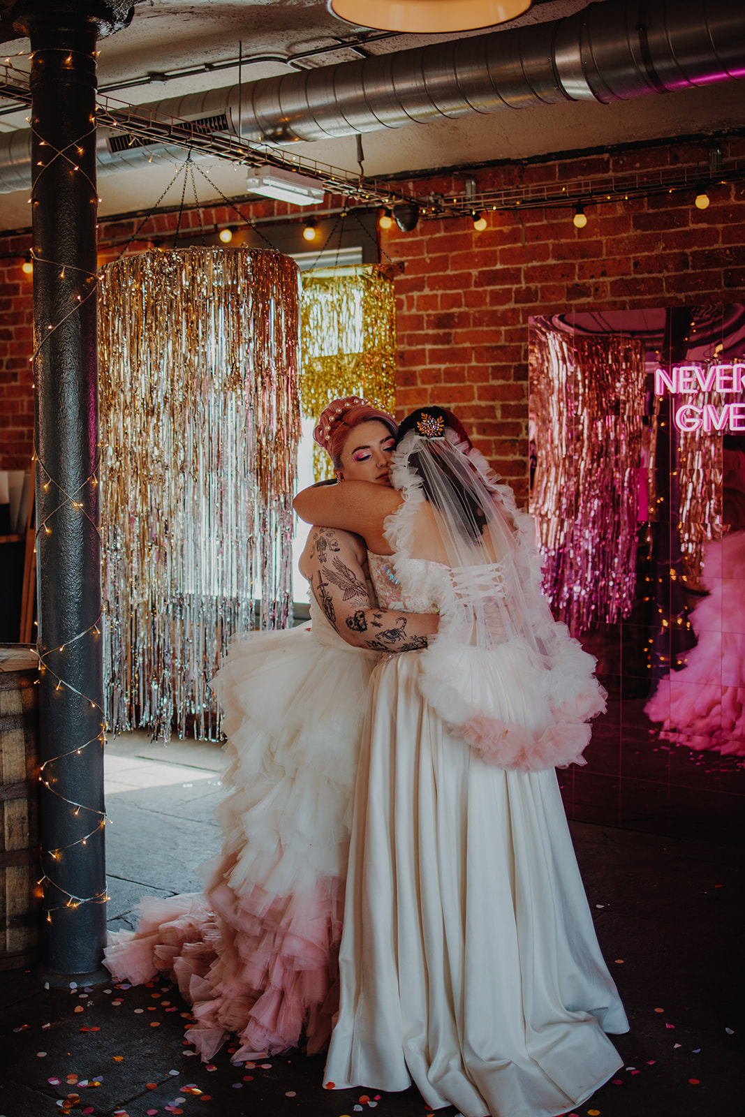 two brides hugging. One wears pink and white tule dress, the other a pink and white tule veil to coordinate