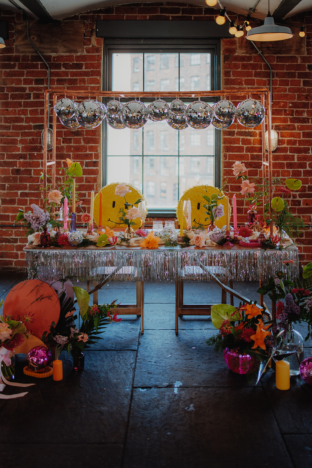 couples wedding breakfast table with glitter ball canopy, silver tassels, smily face piñatas and vibrant flowers