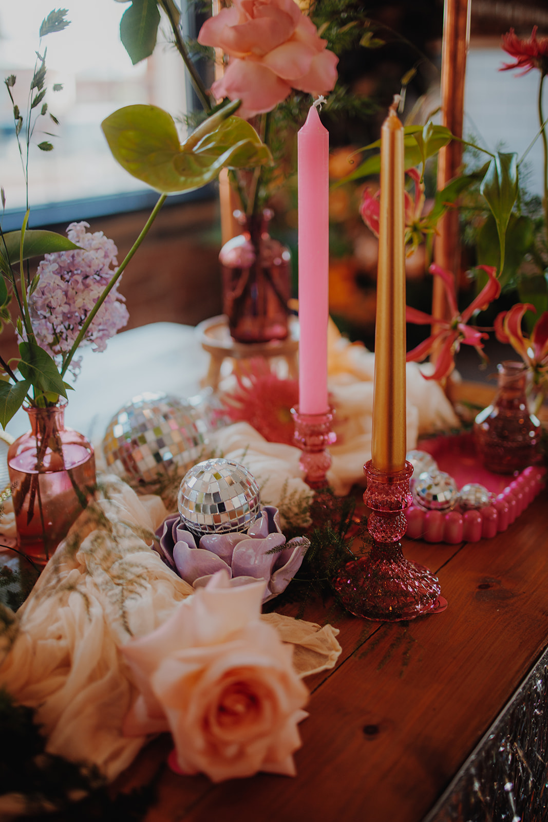 wedding breakfast table close up of colourful glass candle stick, flower candle holders and disco balls