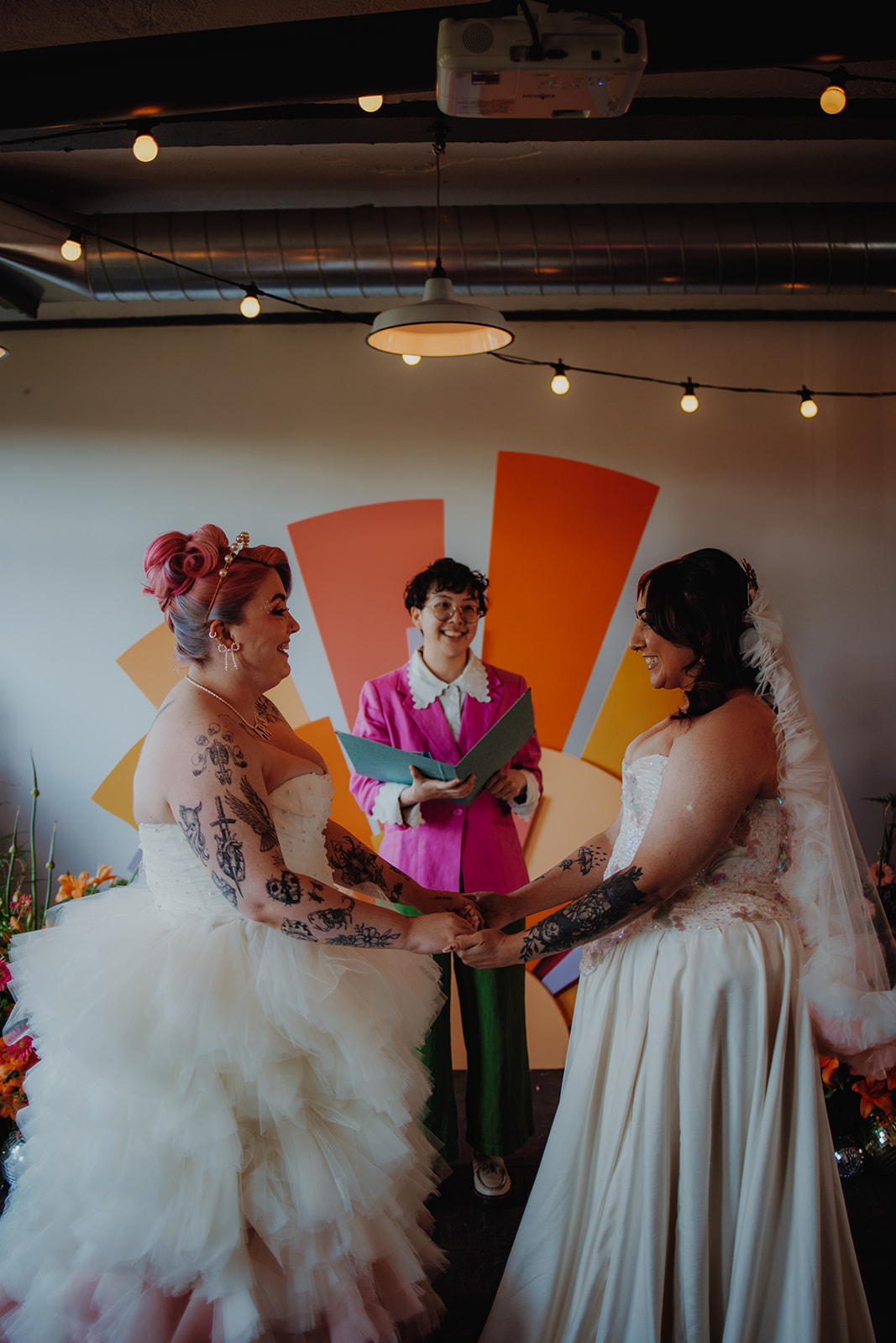 celebrant standing in front of sunshine wedding backdrop delivering a individualised ceremony to the couple wearing handmade wedding outfits in front.