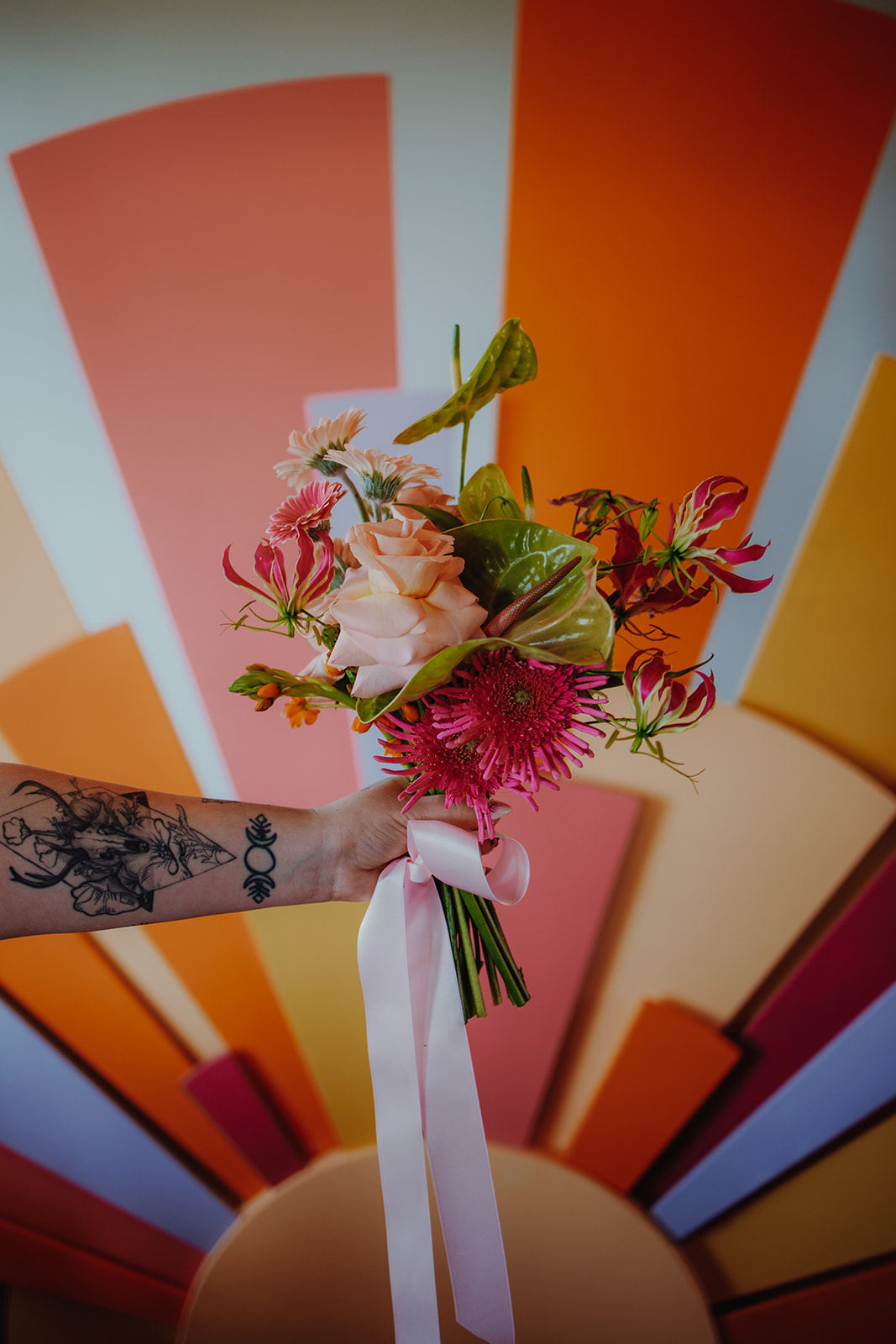 bright pink and green alternative wedding bouquet held in front of colourful sunshine ceremony backdrop
