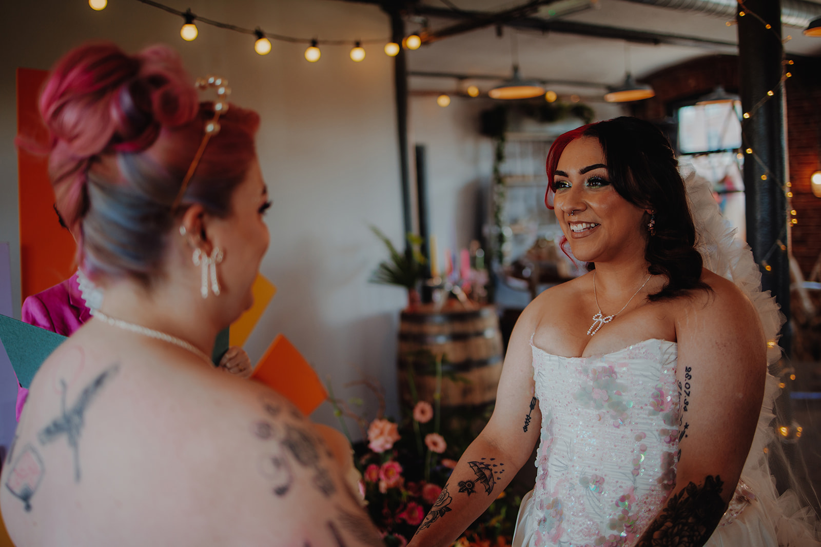 Two brides looking at each other during celebrant led wedding ceremony. Both brides wear handmade wedding outfits
