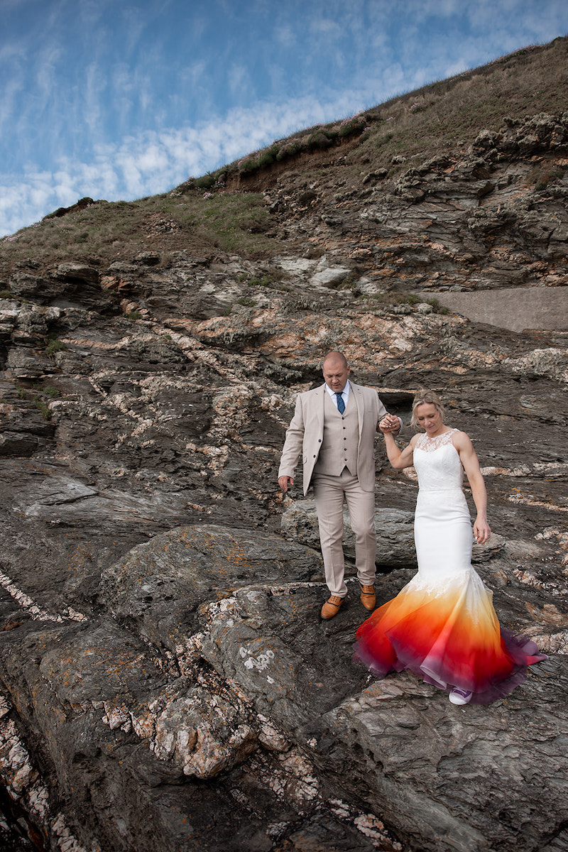 Bride and groom descending the rocks on the Cornish coast as part of their micro elopement portraits