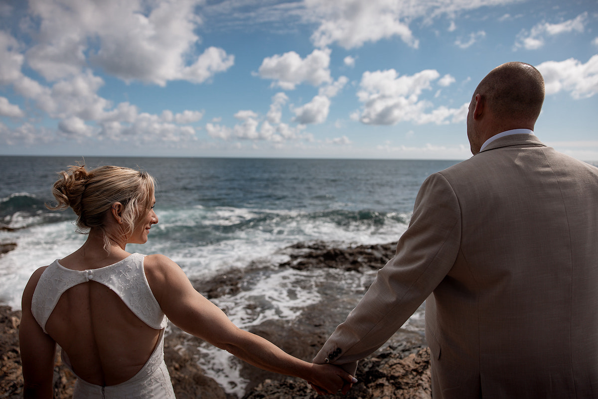Bride and groom holding hands looking out to sea on their micro wedding elopement