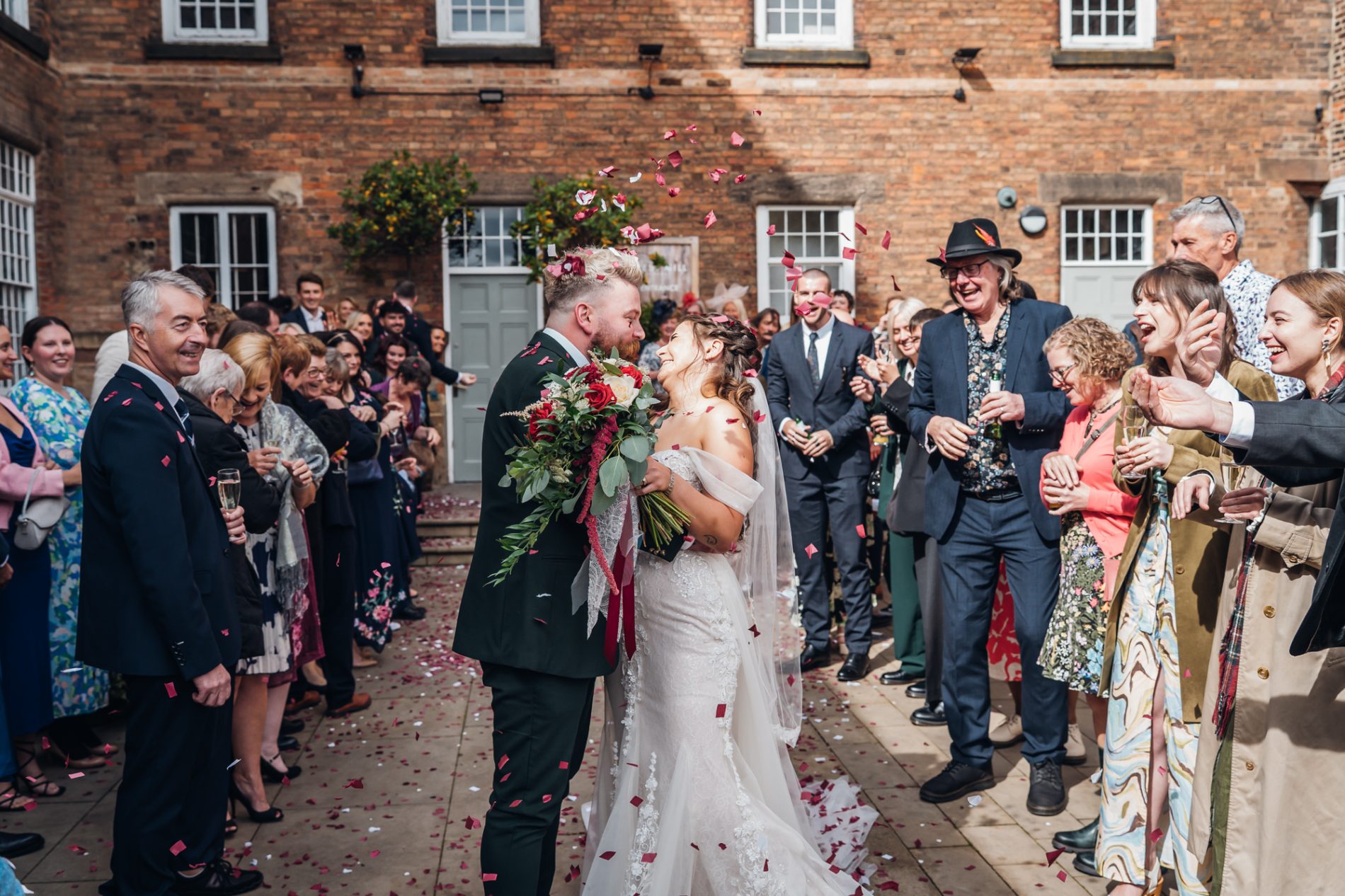 bride and groom hug between two rows of gusts who are throwing real rose petal confetti