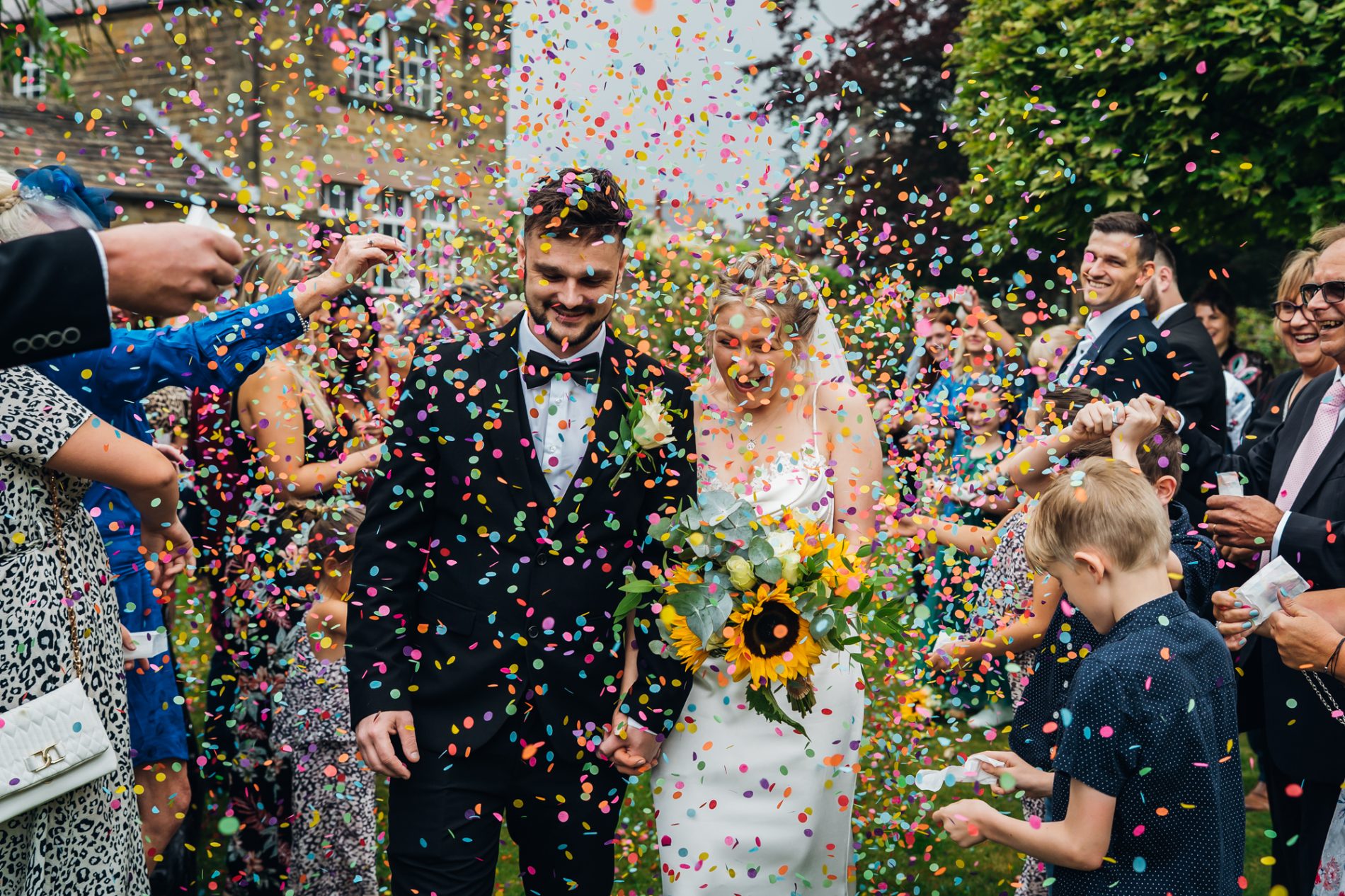 couple walk through brightly coloured tissue confetti tunnel