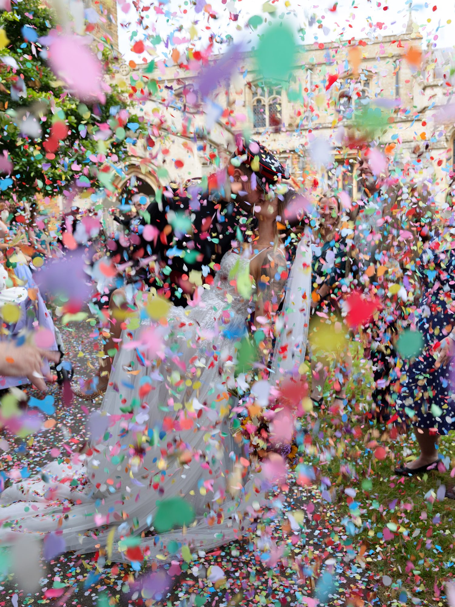 bride and groom dressed in military wear are just visible through pastel rainbow tissue wedding confetti with church in the background