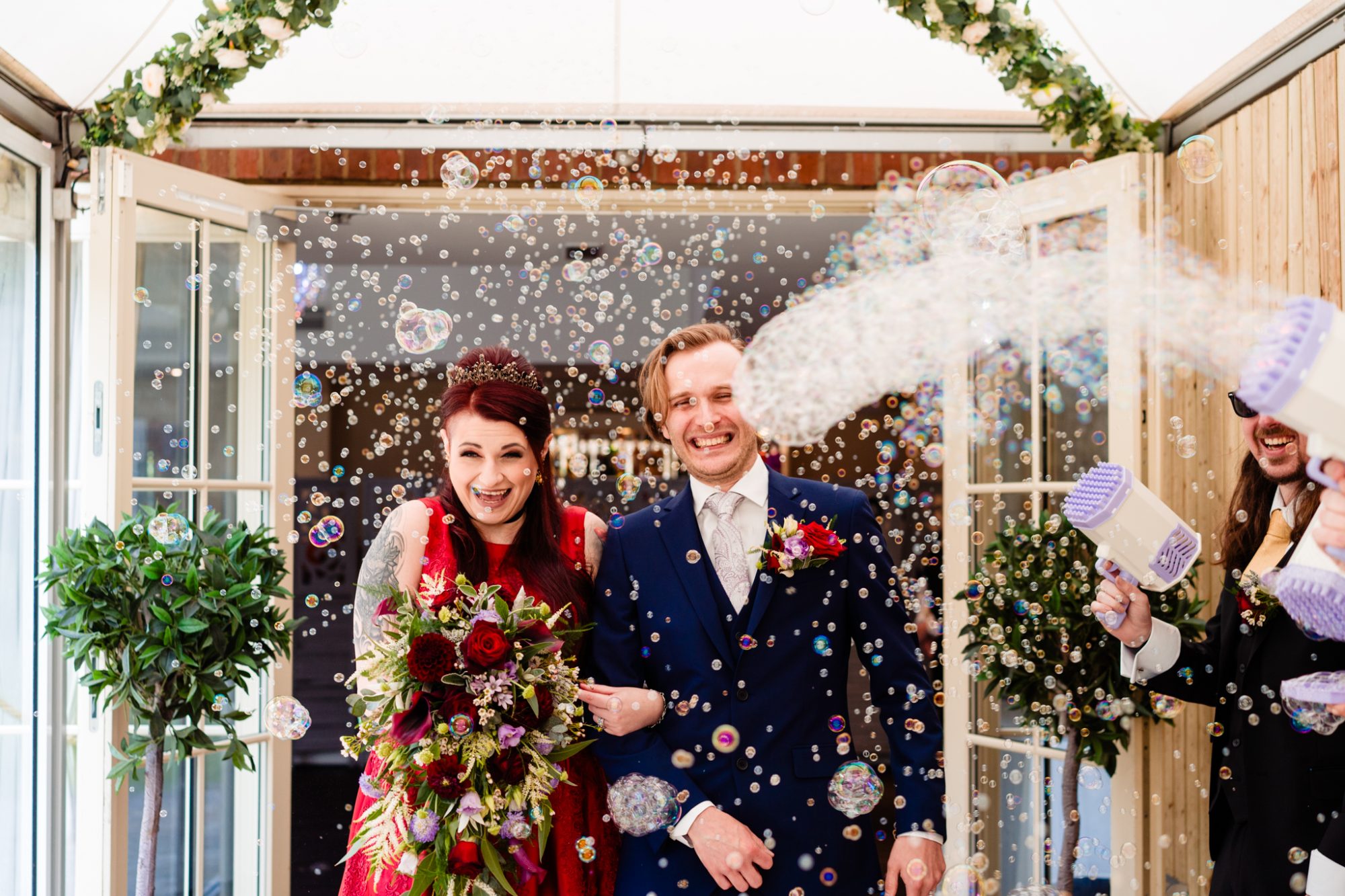 bride and groom walk out of ceremony room into a flurry of bubbles with bubble guns as alternative wedding confetti