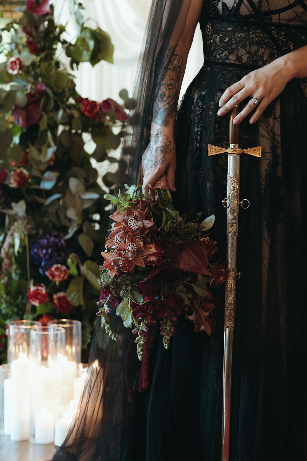 close up of alternative wedding bouquet featuring burgundy orchids. The bride also holds a sword