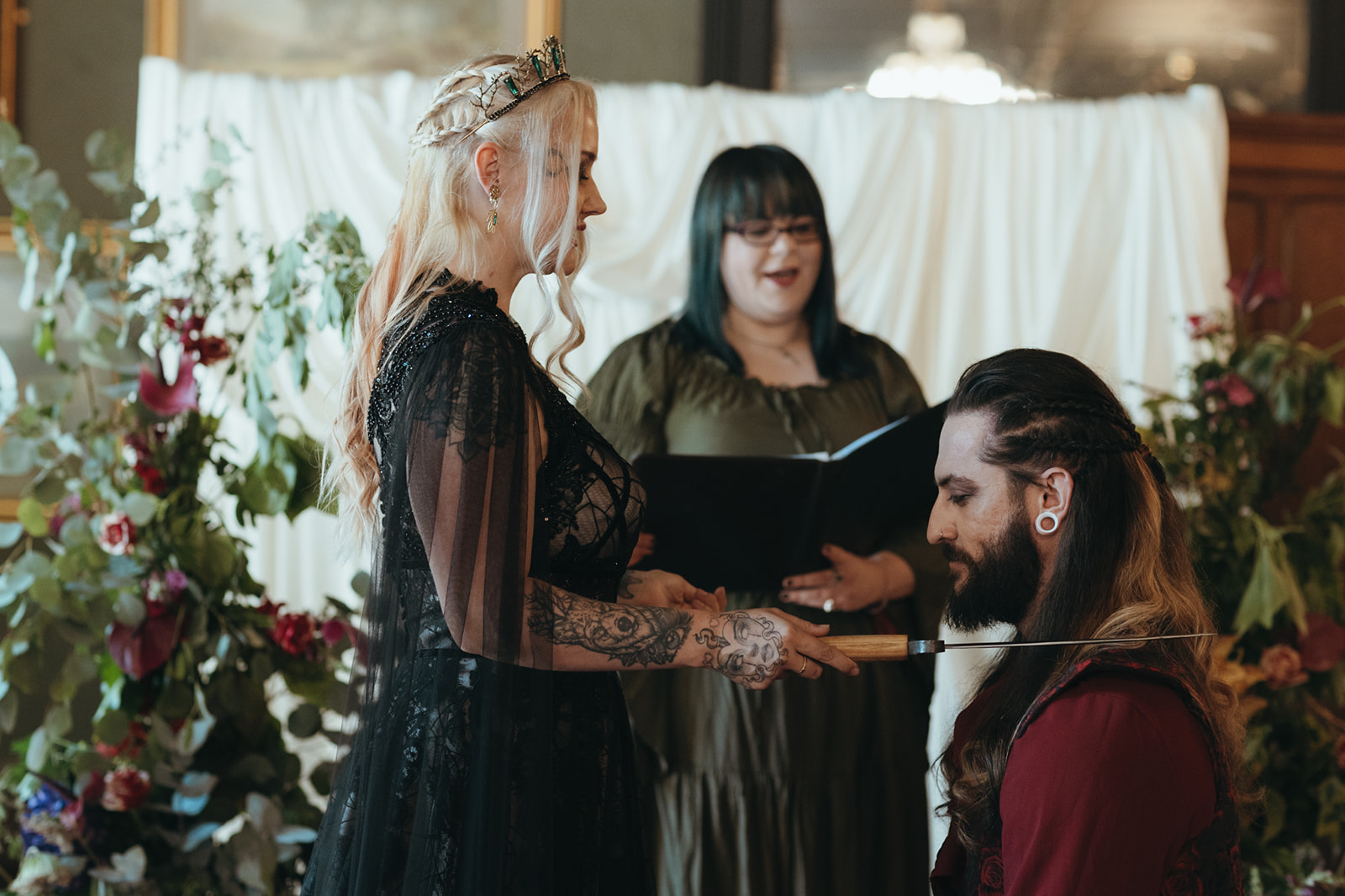 the bride tapping the shoulder of her kneeling gothic groom with a sword as part of celebrant led castle wedding
