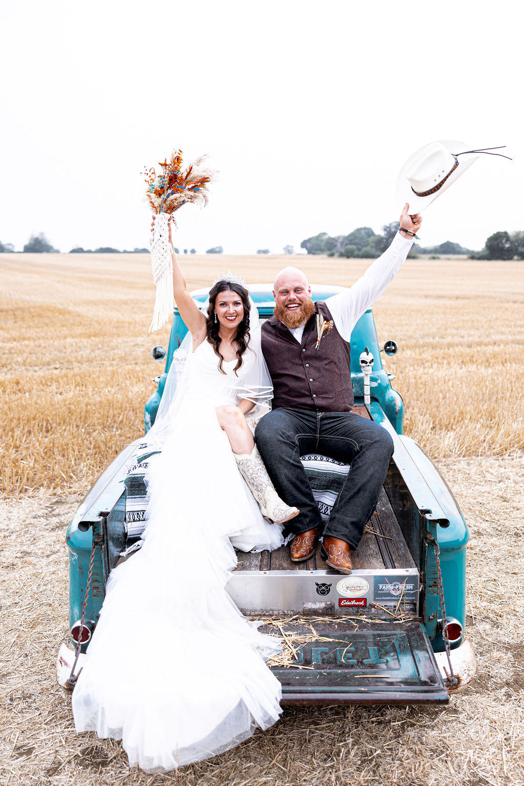 bride wearing cowboy boots and groom wearing western inspired outfit sit in the back of Chevy van wedding transport