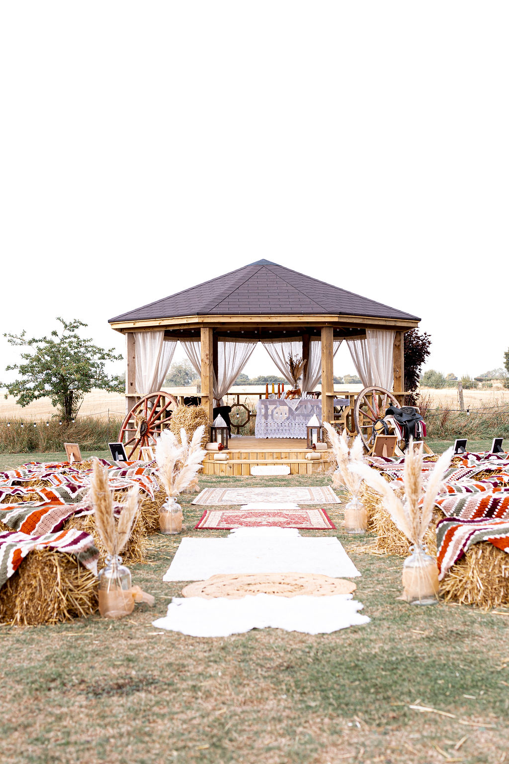 view of the hand build band stand for the wedding ceremony, rug aisle and hay bale seating for guests for rustic American Dream Wedding