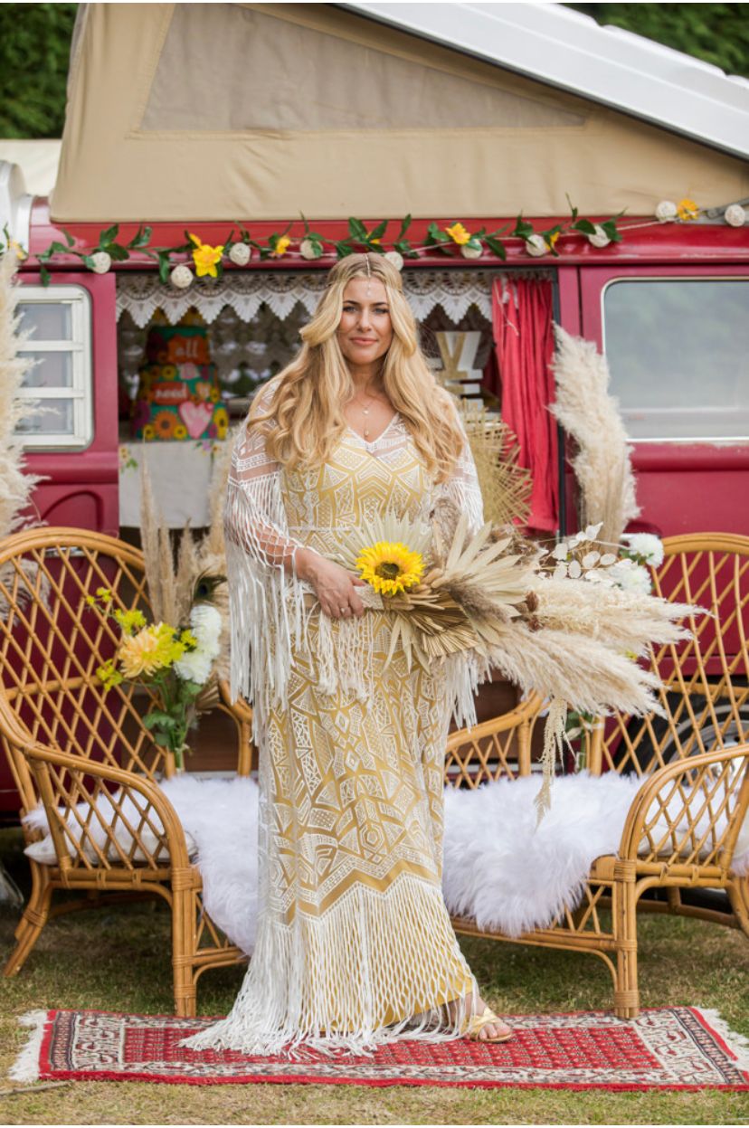 bride wearing boho macrame style dress holding dried flower bouquet in front of boho camper van for festival wedding