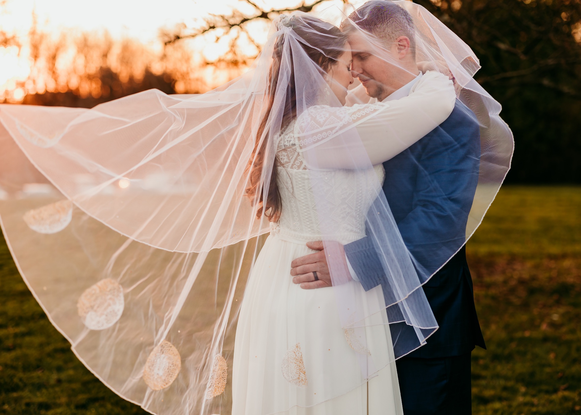 bride and groom pose for a loving photo with the brides veil draped over both of them. Veil made by holly winter couture.