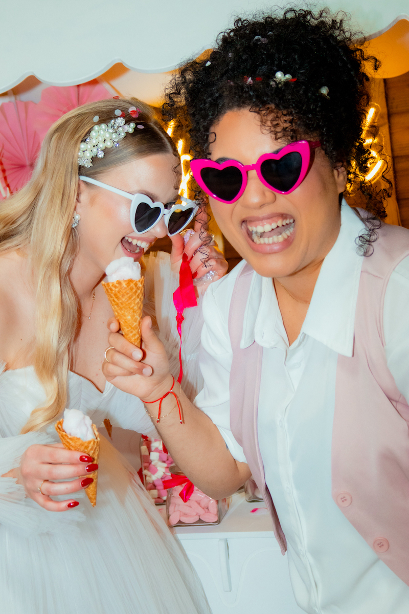 two brides in sunglasses eating sweet treats from the wedding sweet cart