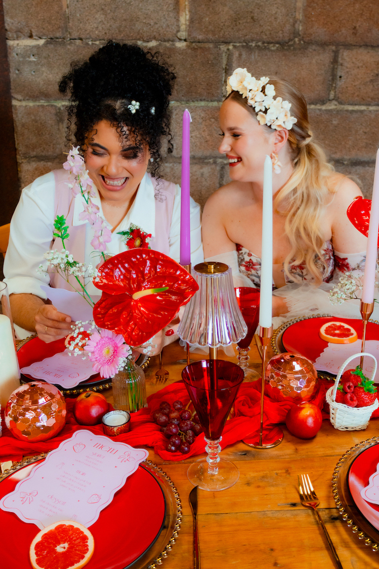 couple sitting at their bright wedding breakfast table looking at pink wedding breakfast menus
