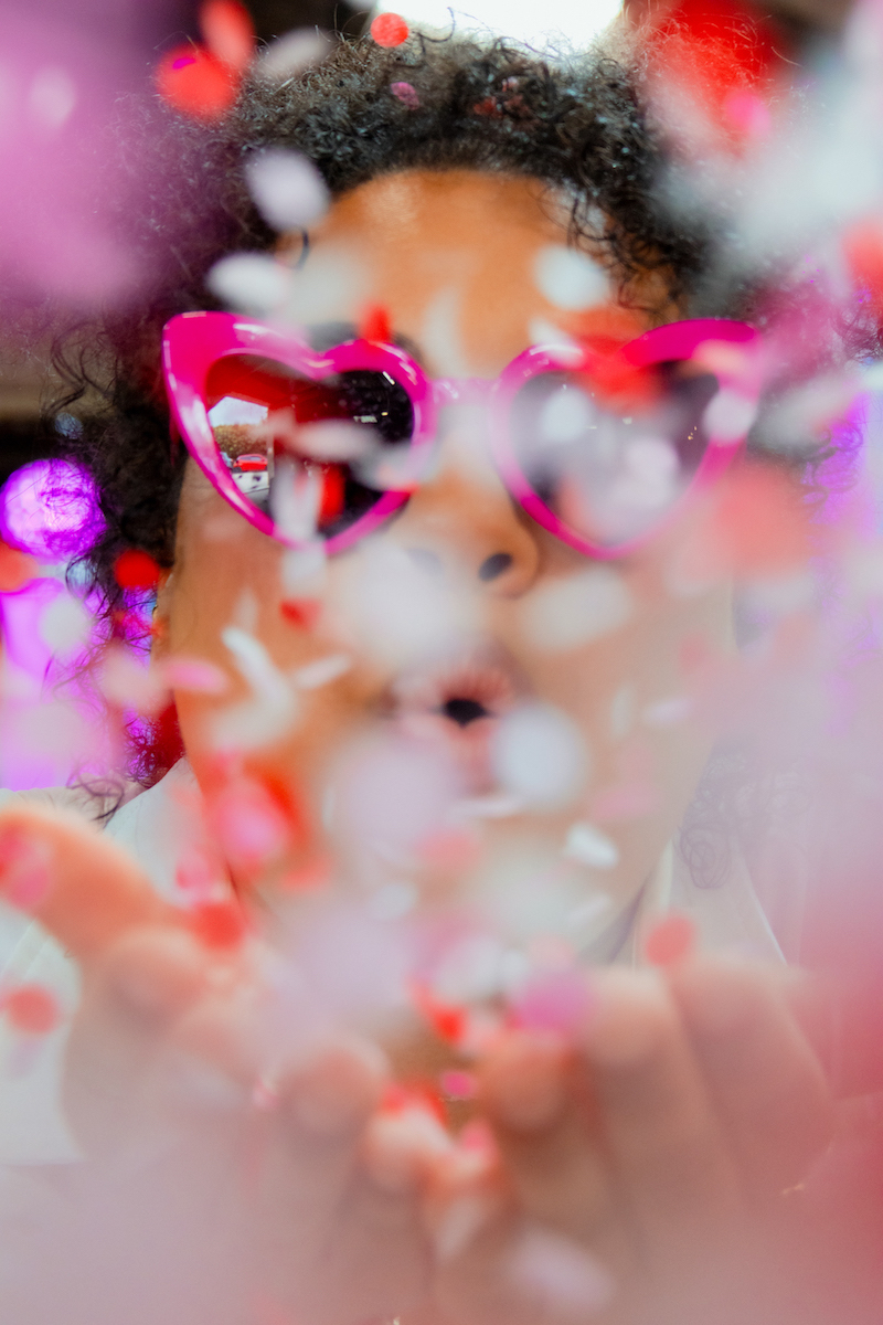 bride wearing pink sunglasses blowing pink and red confetti