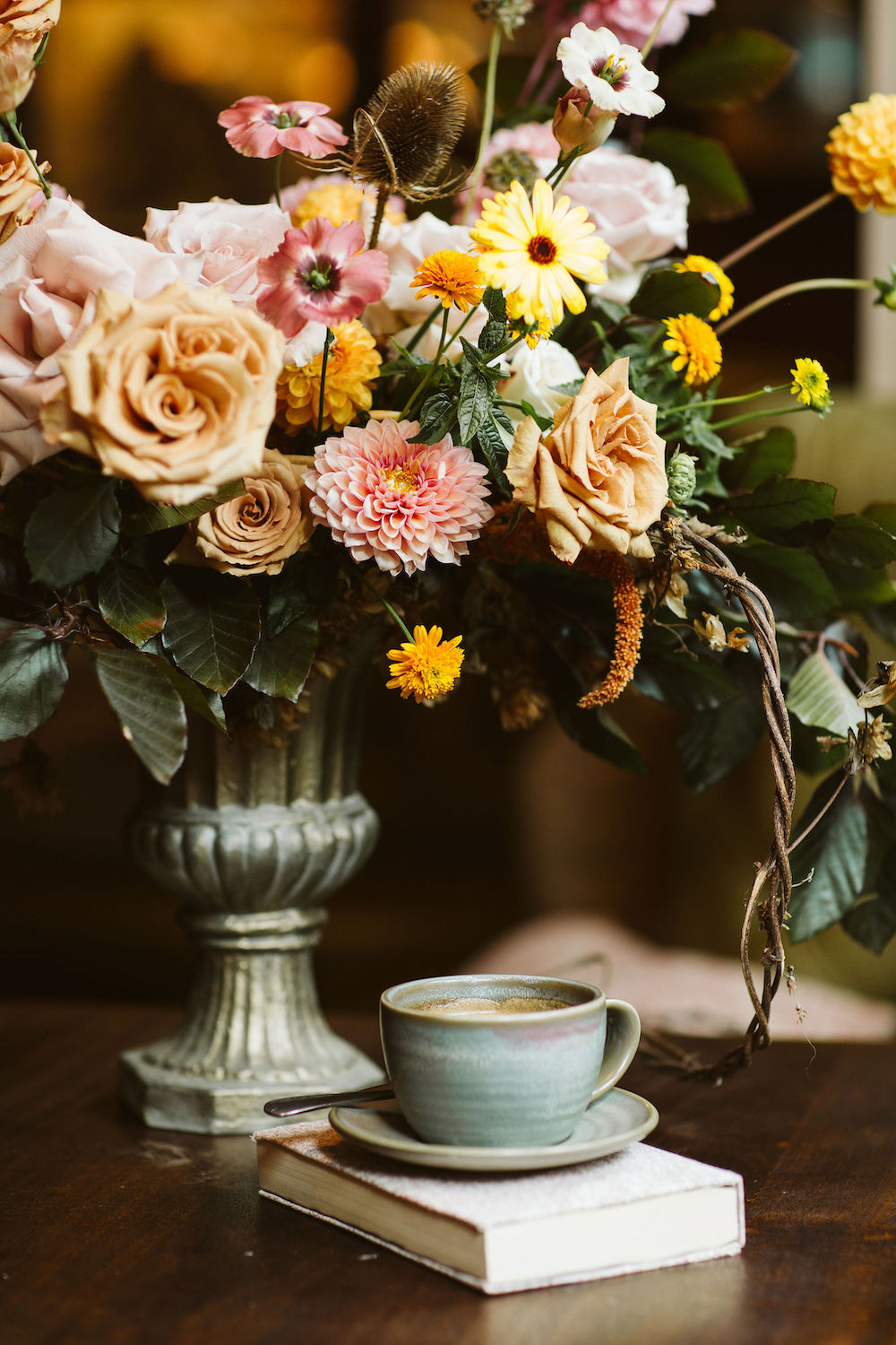 detail shot of a cup of coffee placed on a hard back book with an arrangement of autumn coloured flowers in the background as part of a Gilmore Girls inspired wedding day