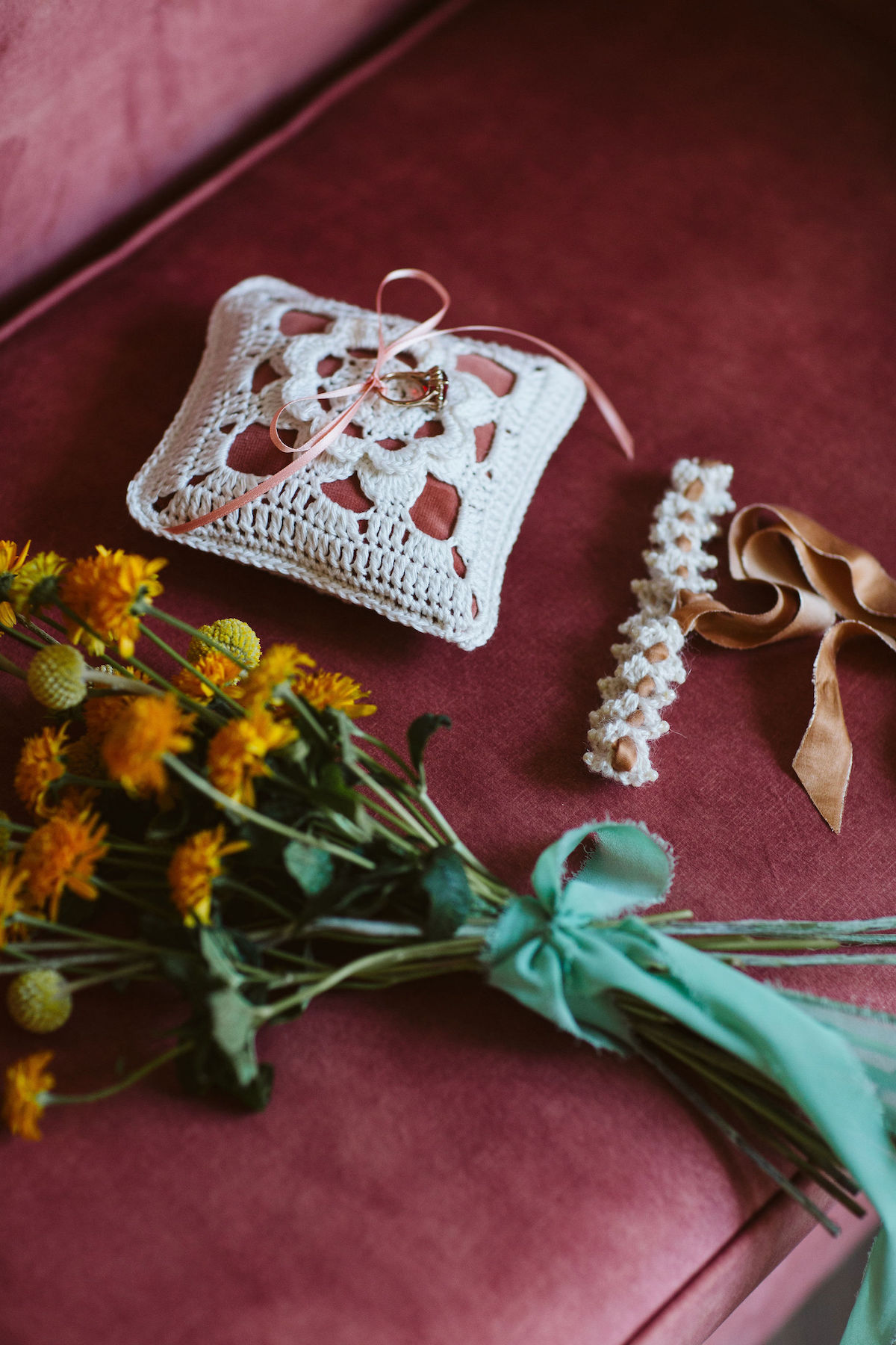 flat lay showing hand crochet ring pillow and wedding garter along side a simple bouquet of yellow flowers