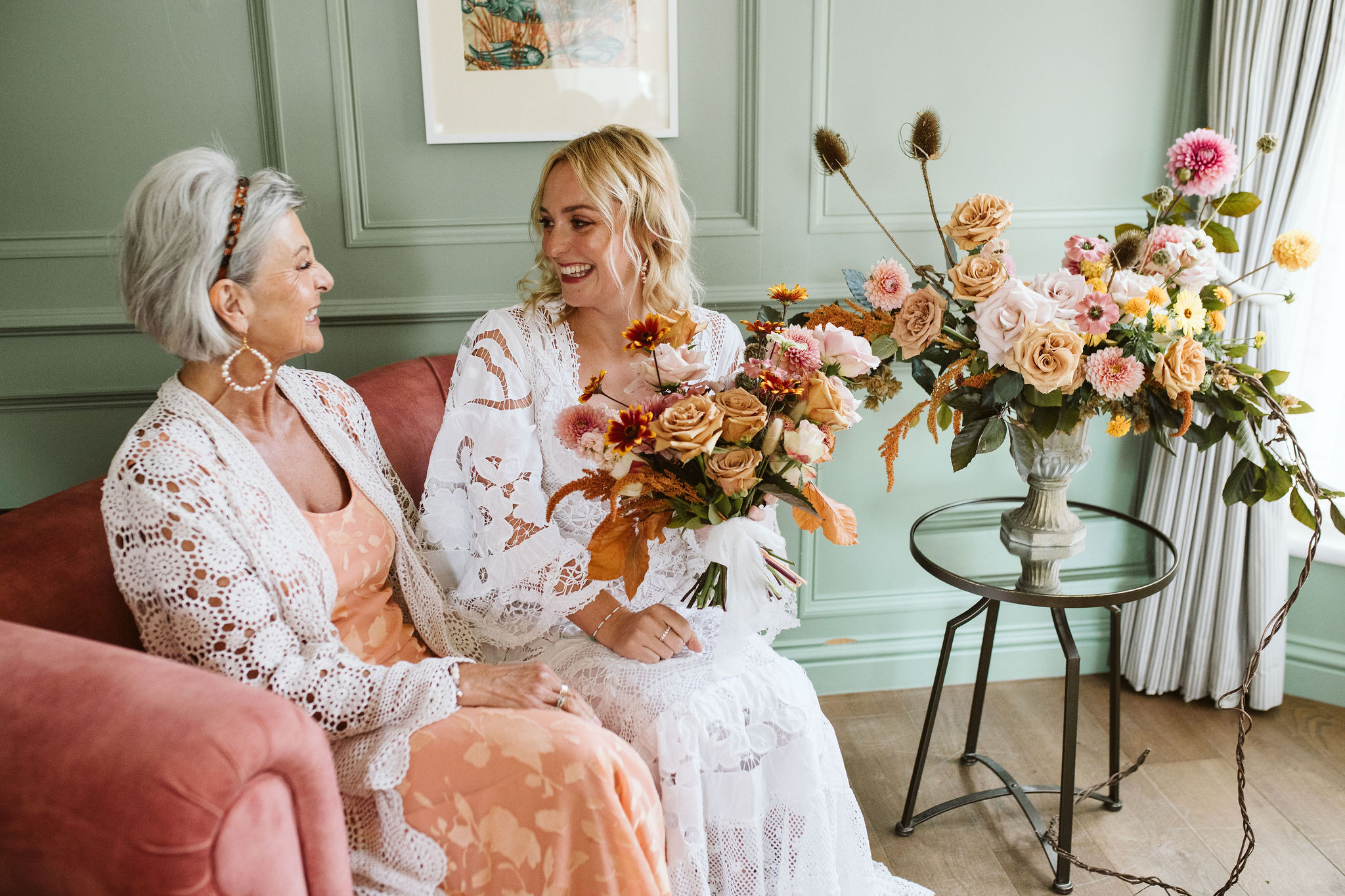 mother and daughter portrait - the pair sit on a sofa. The bride holds a large bouquet of Autumn coloured British grown flowers