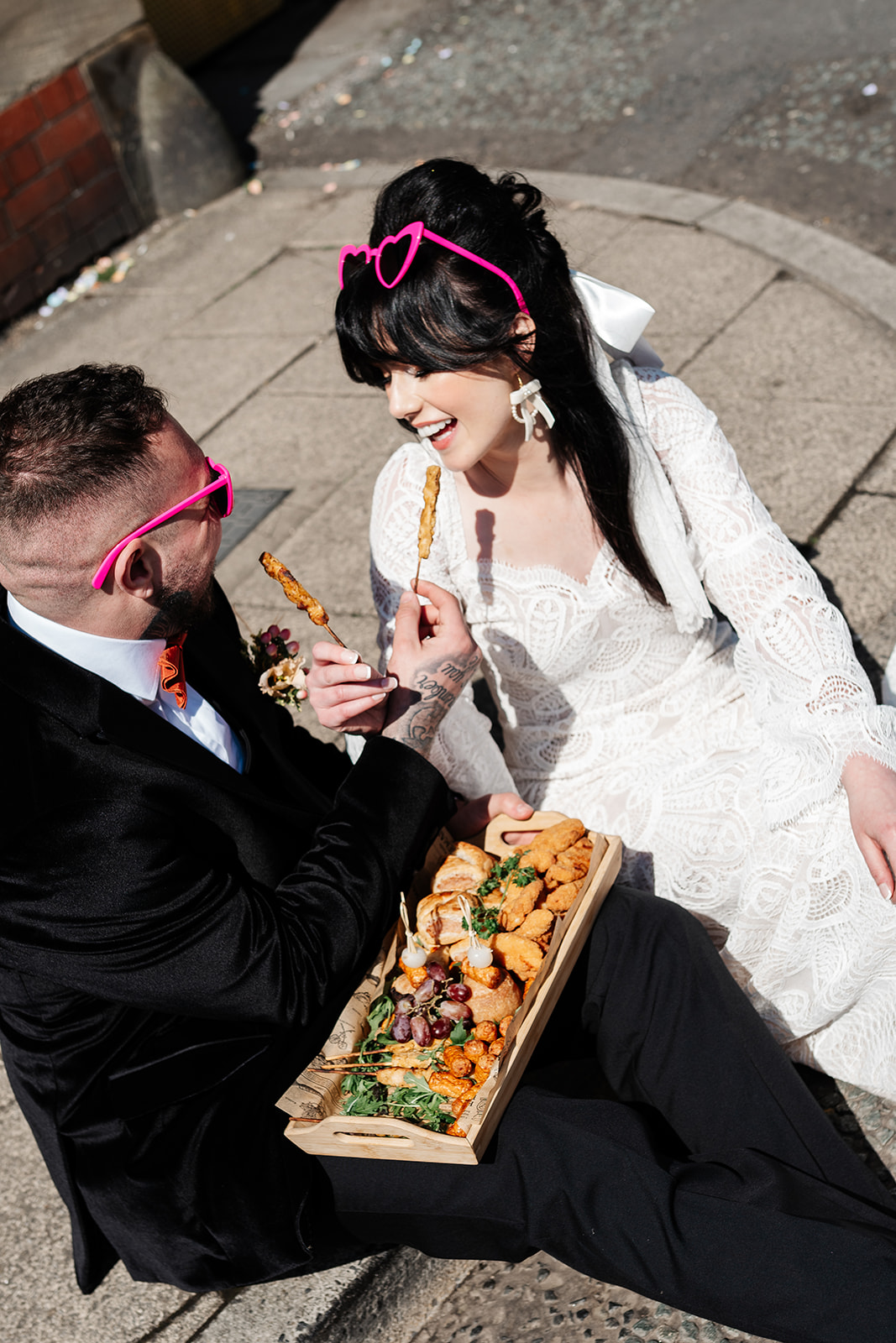 couple sitting in the street eating mini kebabs as part of northern wedding breakfast