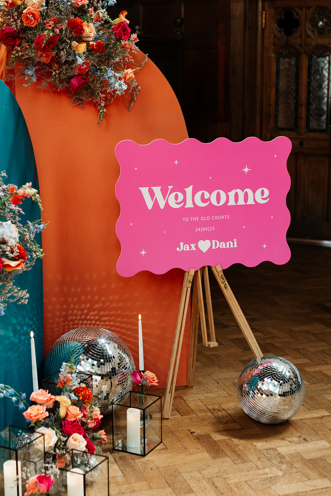 detail shot of wedding welcome sign agains arch backdrop with bright wedding flowers and disco balls