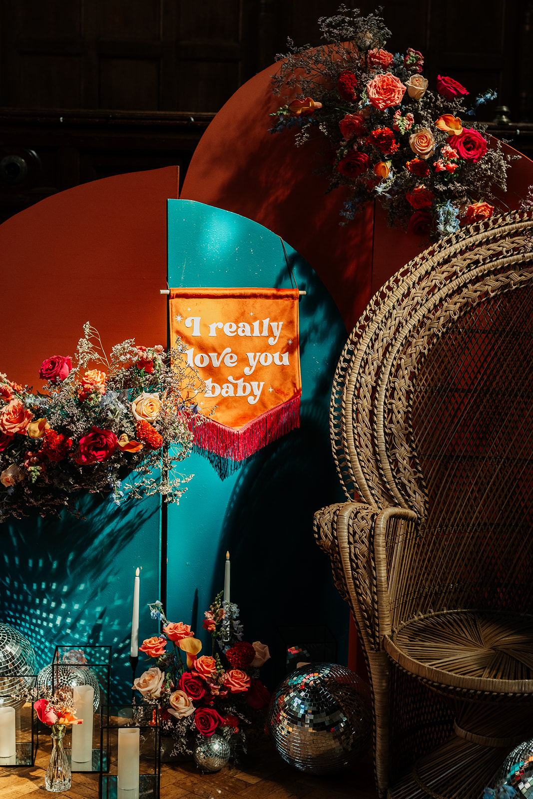 moody photo of light on wedding decor - arch ceremony backdrop, peacock chairs and bright wedding flowers with 'i really love you' banner