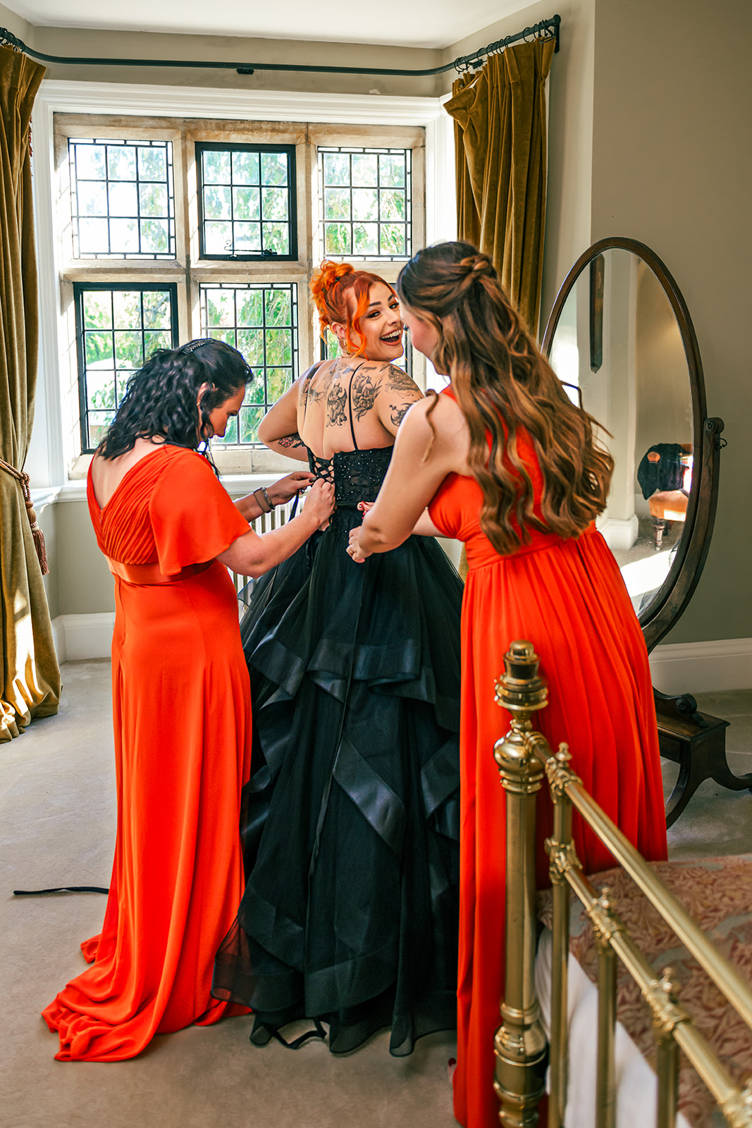 bridesmaids wearing orange help to do up the corset back of the gothic black wedding dress