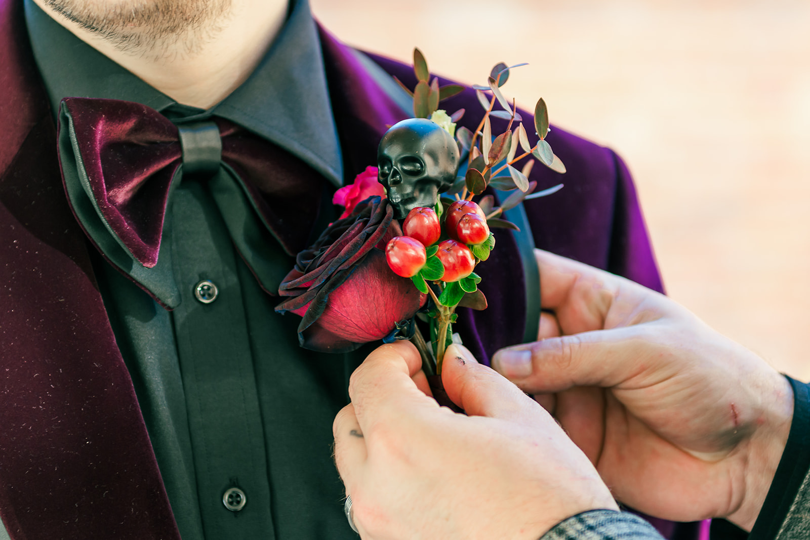 groom having his deep red and orange button hole with black skull attached to his deep purple suit jacket