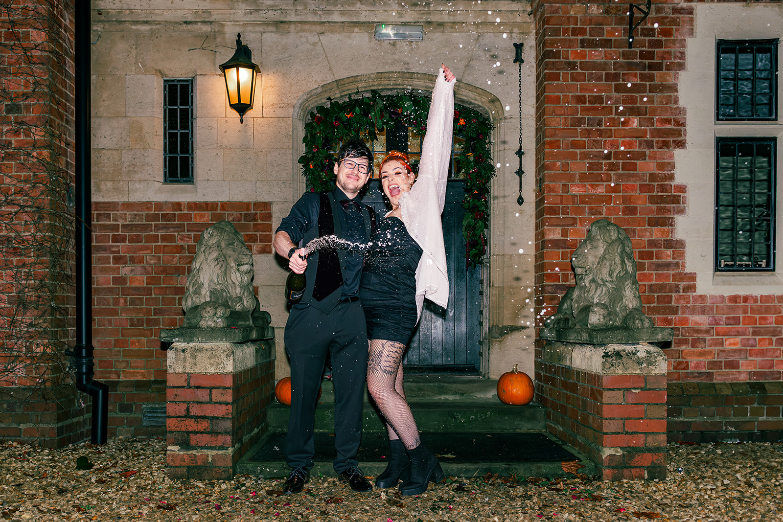 Bride and groom celebrate with a champagne spray. Halloween pumpkin are on the steps of the wedding venue entrance