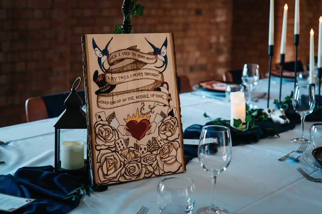 detail shot of an Alice in wonderland and tattoo inspired pyrography wedding sign stood on the wedding breakfast table