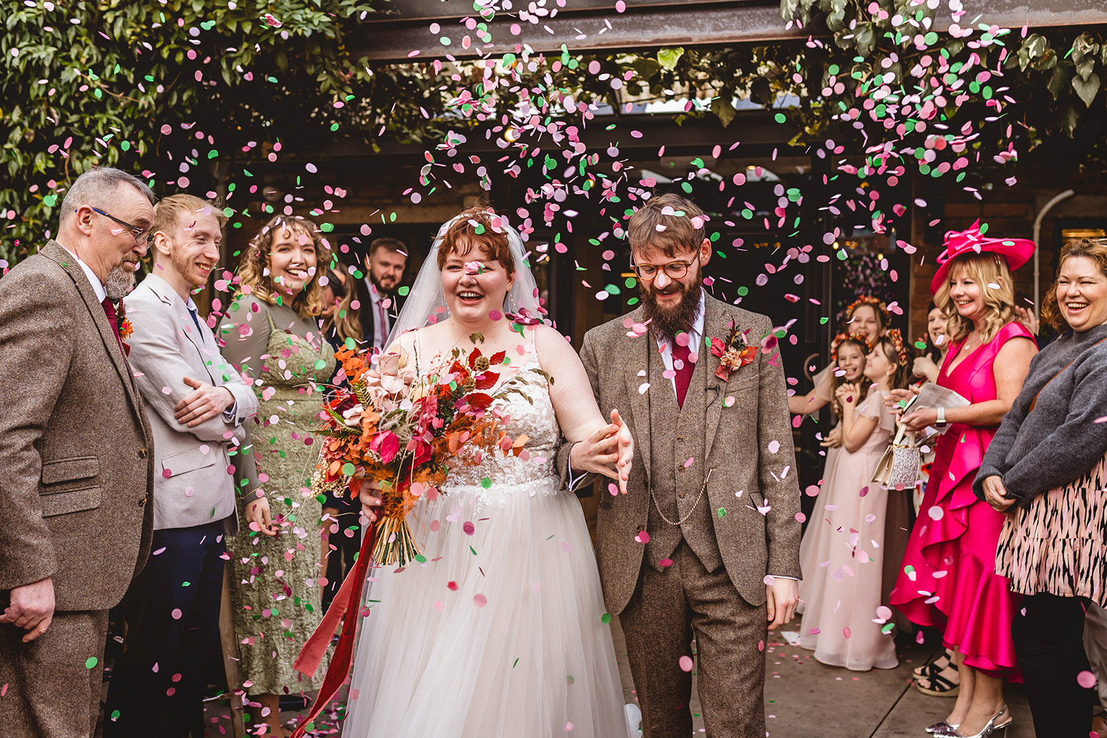 Bride and groom walk between an aisle of wedding guests while being showered in green and pink confetti