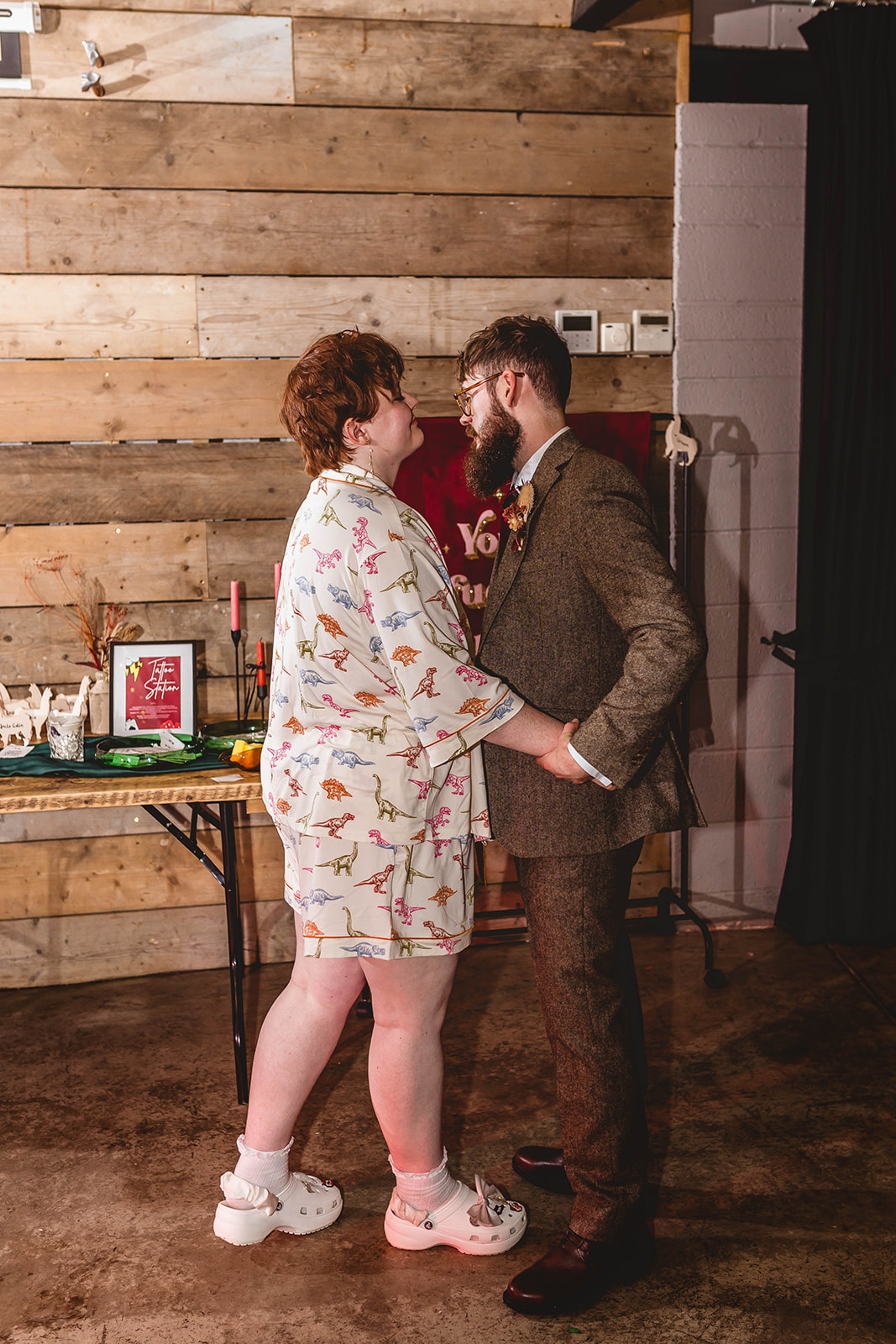 bride and groom hugging during the evening party. The bride is wearing her dinosaur pjs and wedding crocs