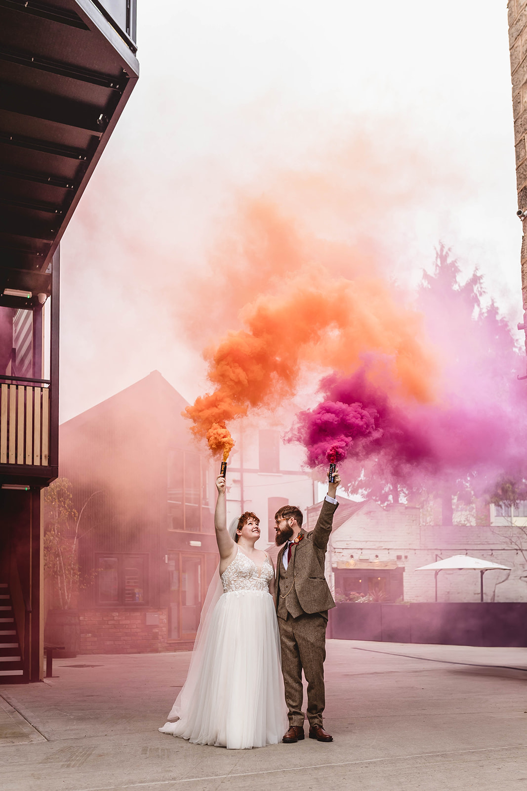 bride and groom outside their dry hire wedding venue holding pink and orange smoke bombs