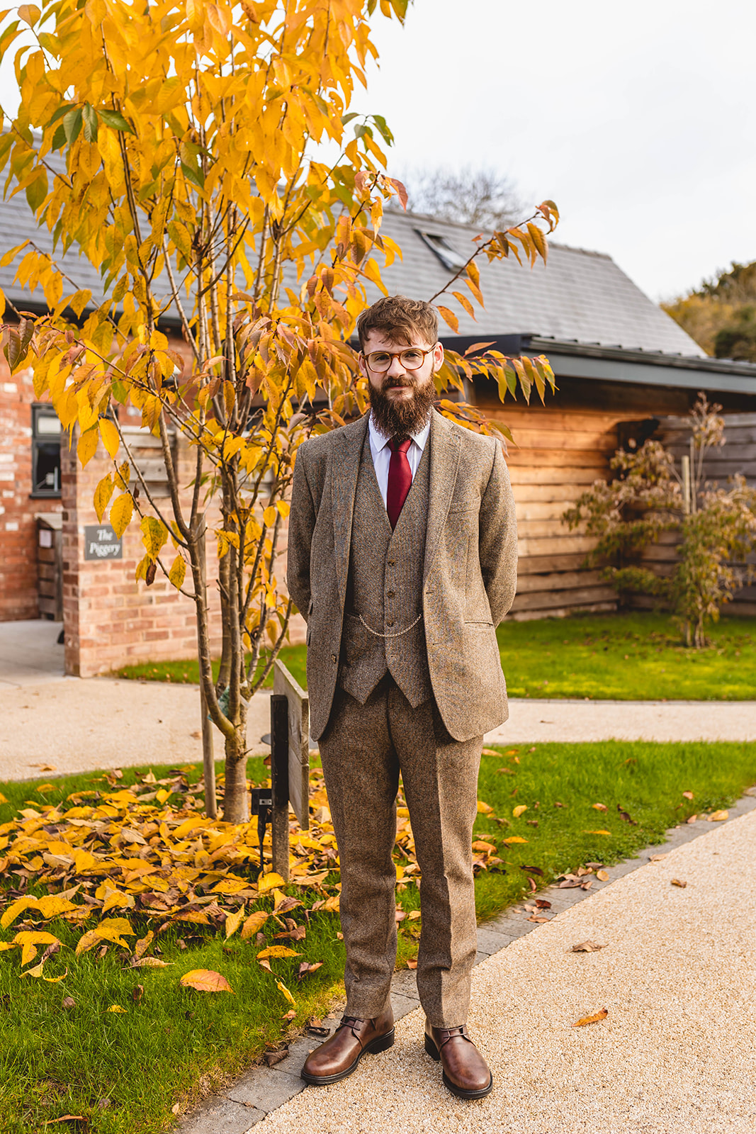groom portrait next to yellow autumn leaved tree. Groom wears brown three piece tweed suit