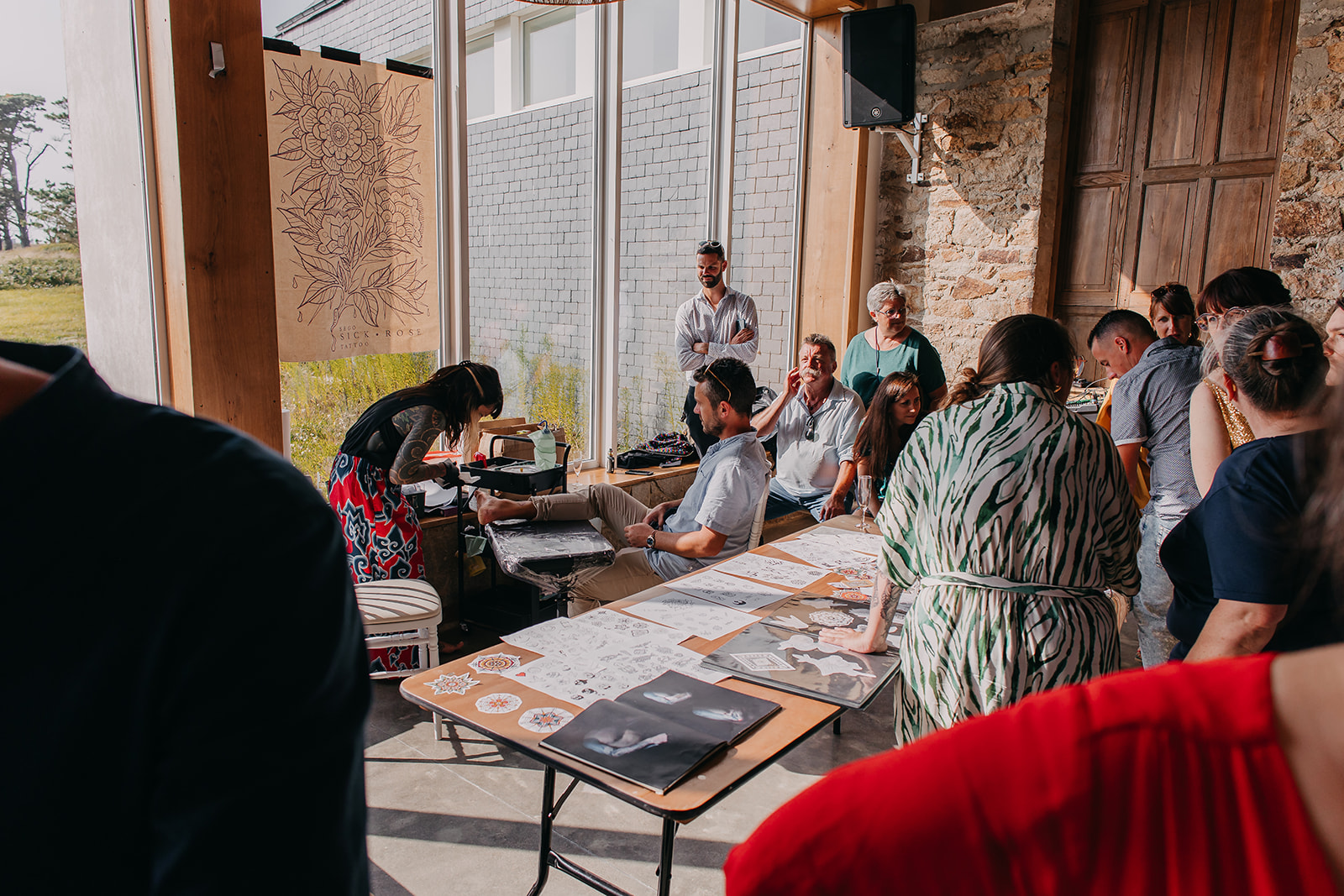 wedding guests wait to receive their wedding day tattoo. A man is sat a the tattoo artist bench having a tattoo on his foot