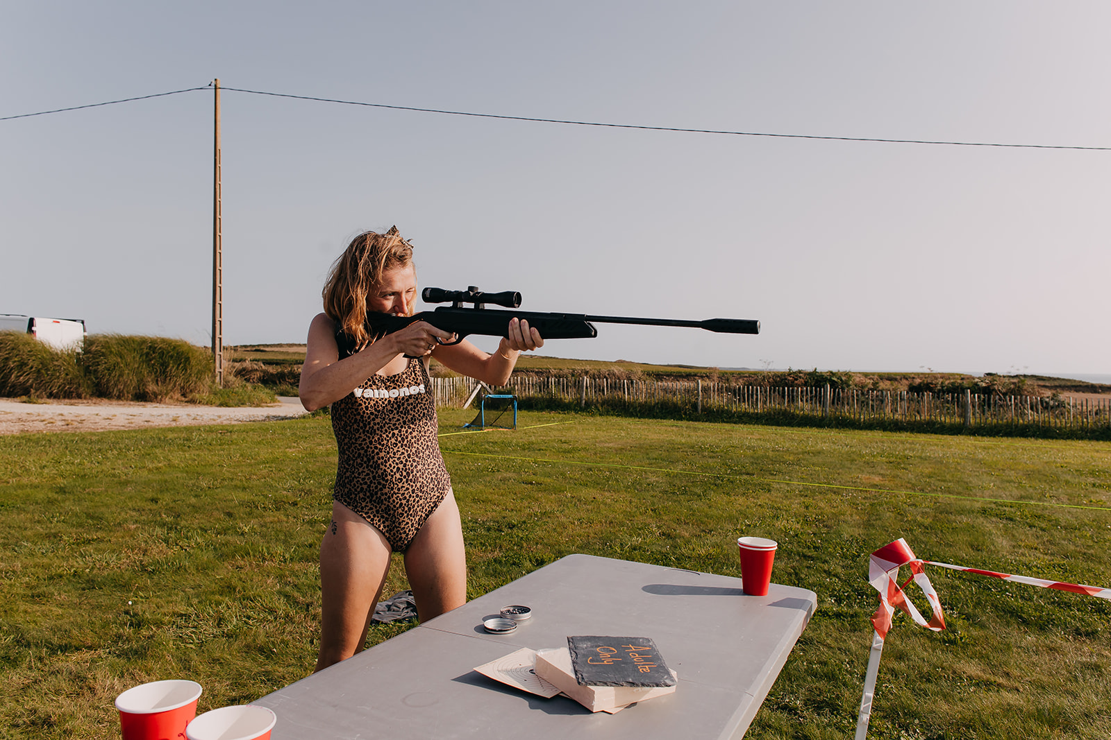 Wedding guest wearing a leopard print swimsuit stands with an air rifle as part of the guest entertainment at an unconventional french wedding
