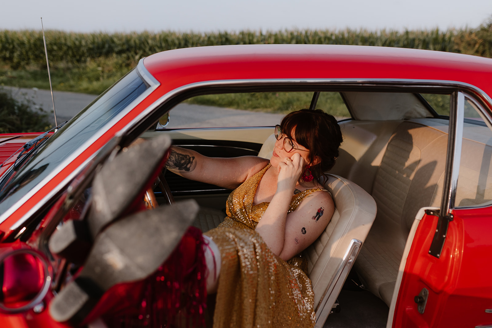 bridal portrait of bride wearing gold dress sat in a red car at sunset