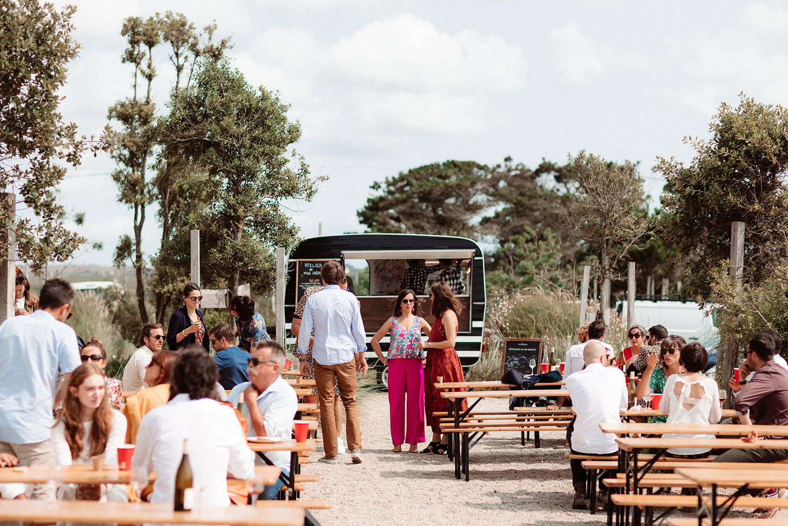 wedding guests sitting at benches outside a wedding crepe food truck as part of french wedding
