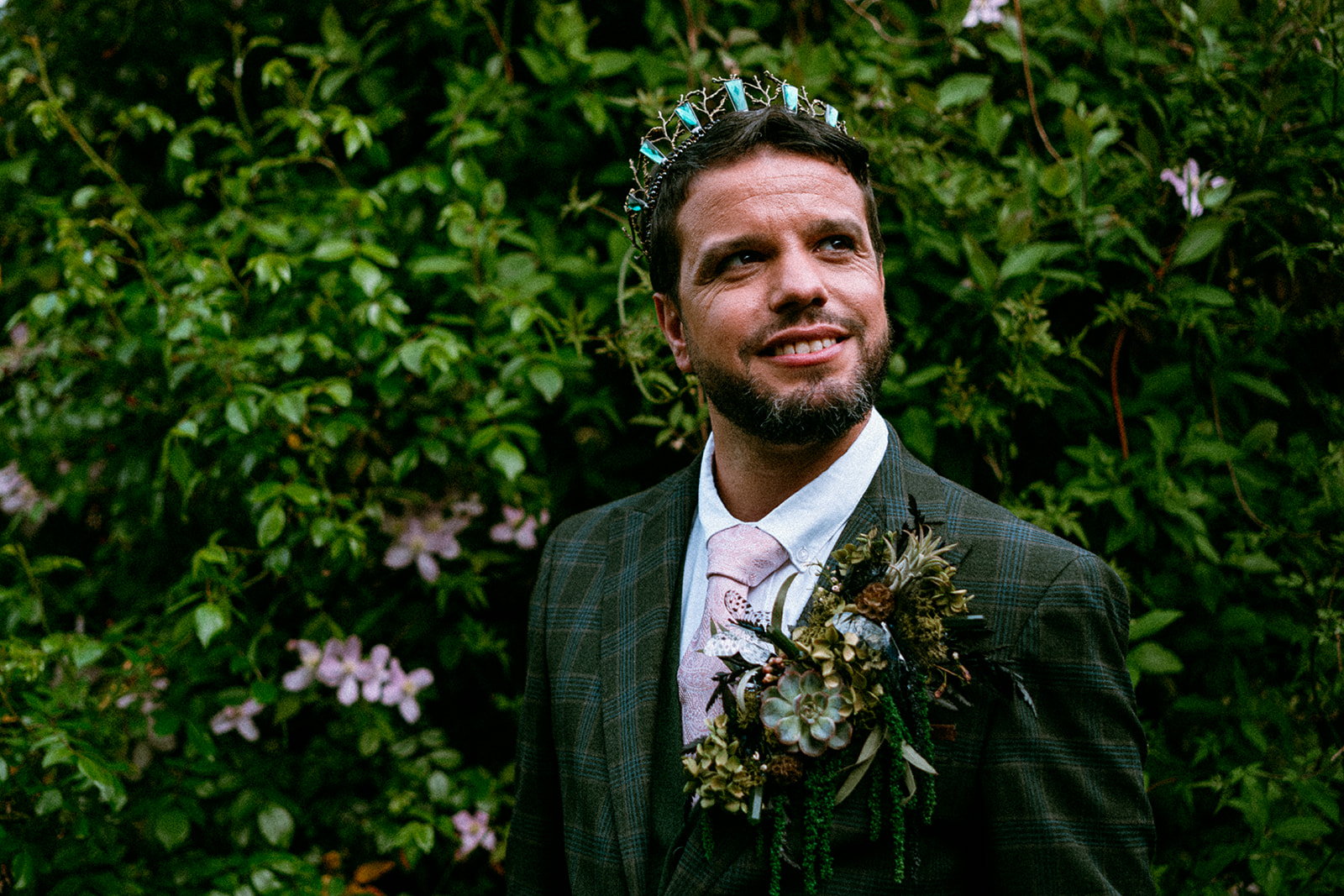 Groom portrait - groom with beard wears green suit with pink tie and statement alternative lapel decoration and emerald green crown in Wicked themed wedding.