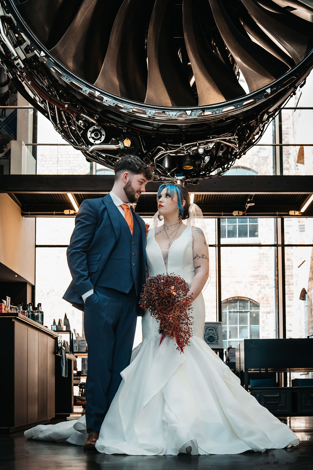 bride and groom stand in front of a huge rolls-royce trent 1000 engine for alternative couple portrait in a museum