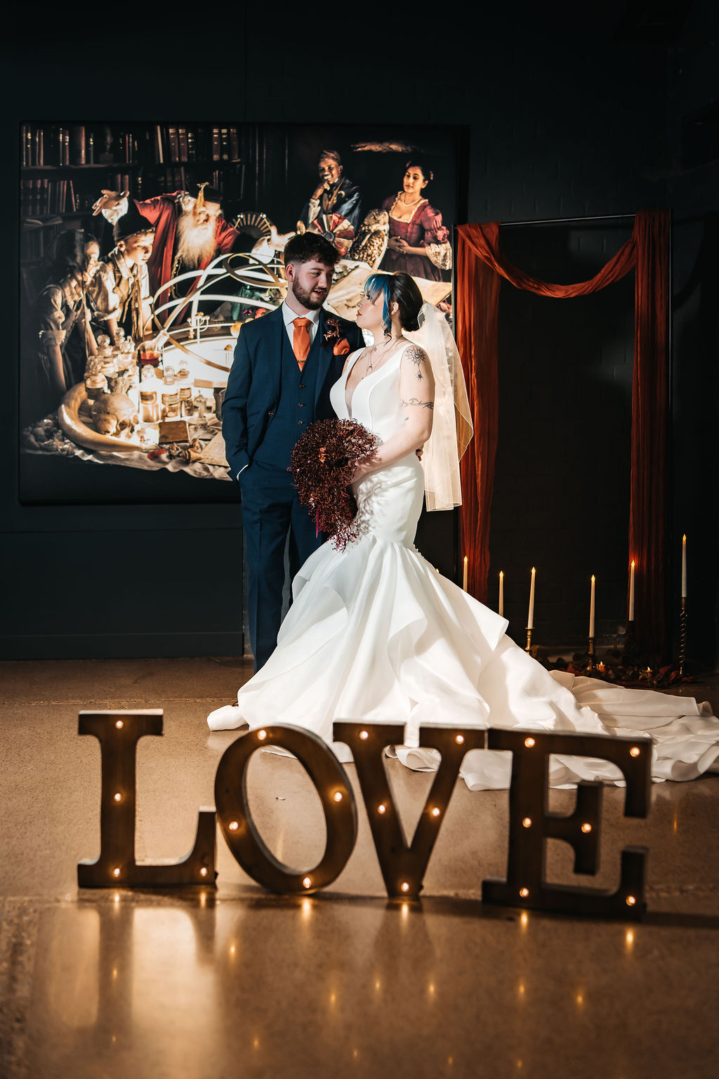 couple portrait in front of a Joseph Wright image with candles and light up love letters as part of a candlelit industrial museum wedding