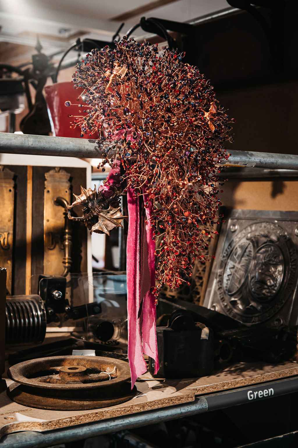 detail shot of copper wire and bead alternative wedding bouquet with dragon handle. The bouquet is displayed on a shelf of industrial artefacts