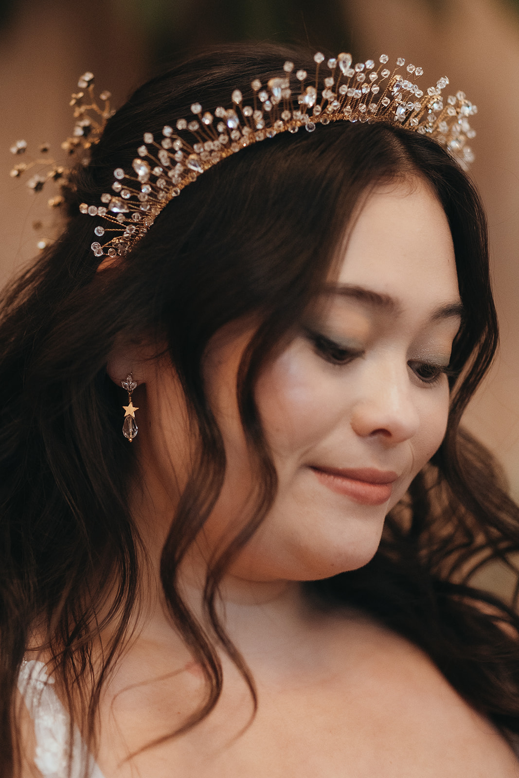 close up shot of a bride who wears crystal drop earrings with stars and a crystal headband crown. Her long dark hair is in soft ringlets.