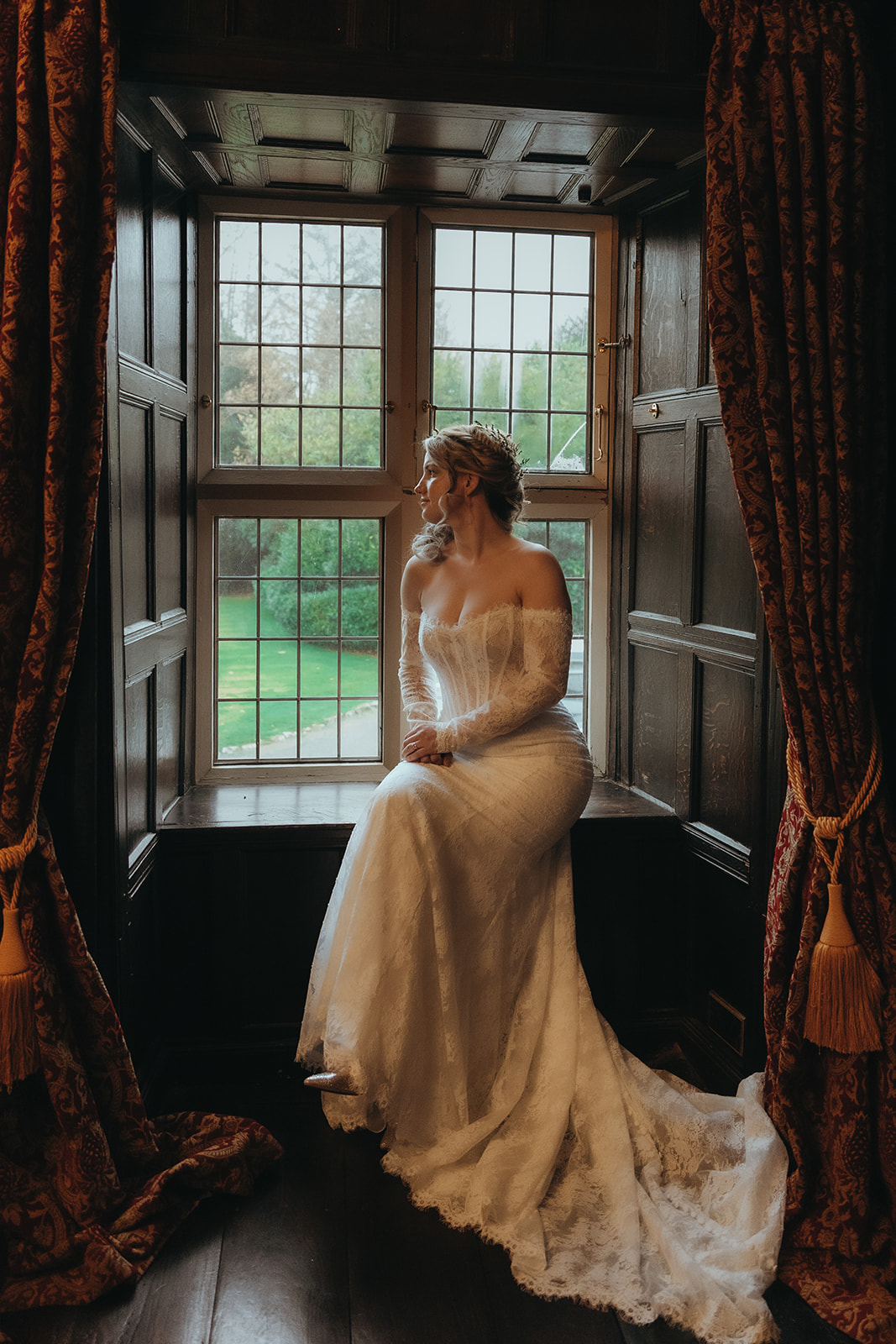 bride wearing structured corset dress sat in the deep wood panelled window seat at a historical wedding venue for Renaissance wedding