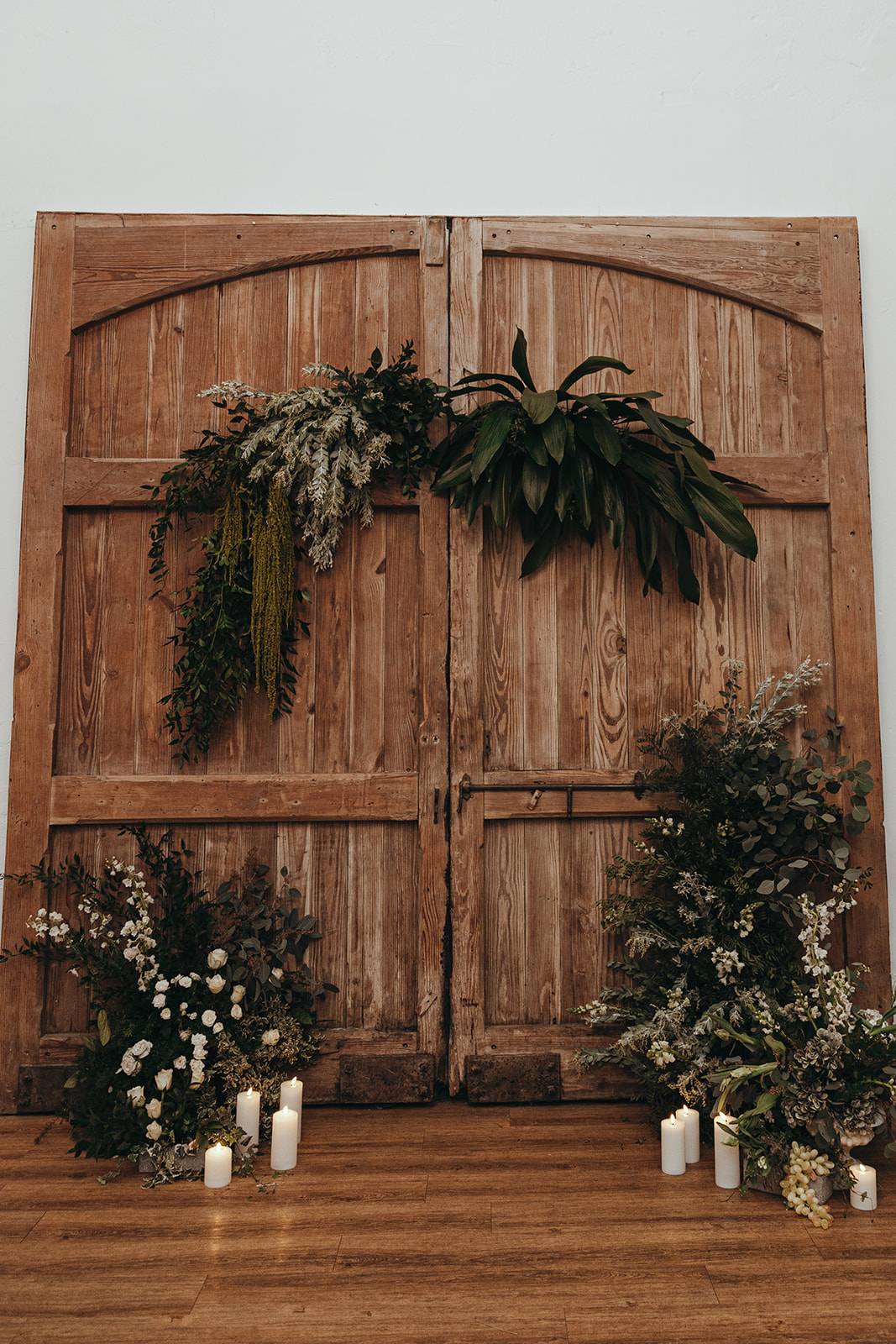 detail shot of the asymmetrical floral arch against large wooden coach hall doors for winter wedding