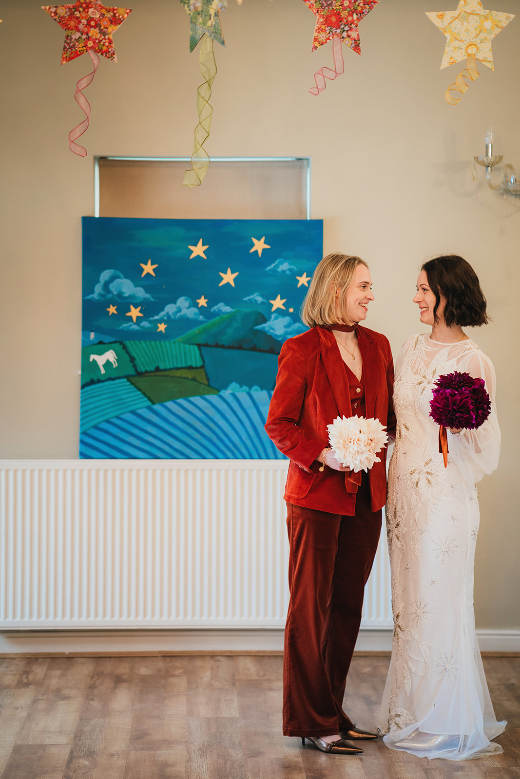 two brides stand beneath handmade stars and in front of a hand painted picture at their slow intentional wedding ceremony