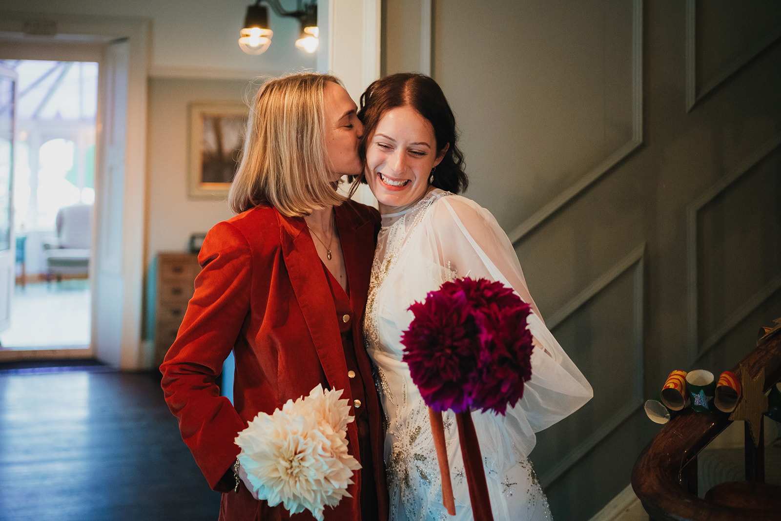bride in red kisses bride in white at their first look on their slow wedding day