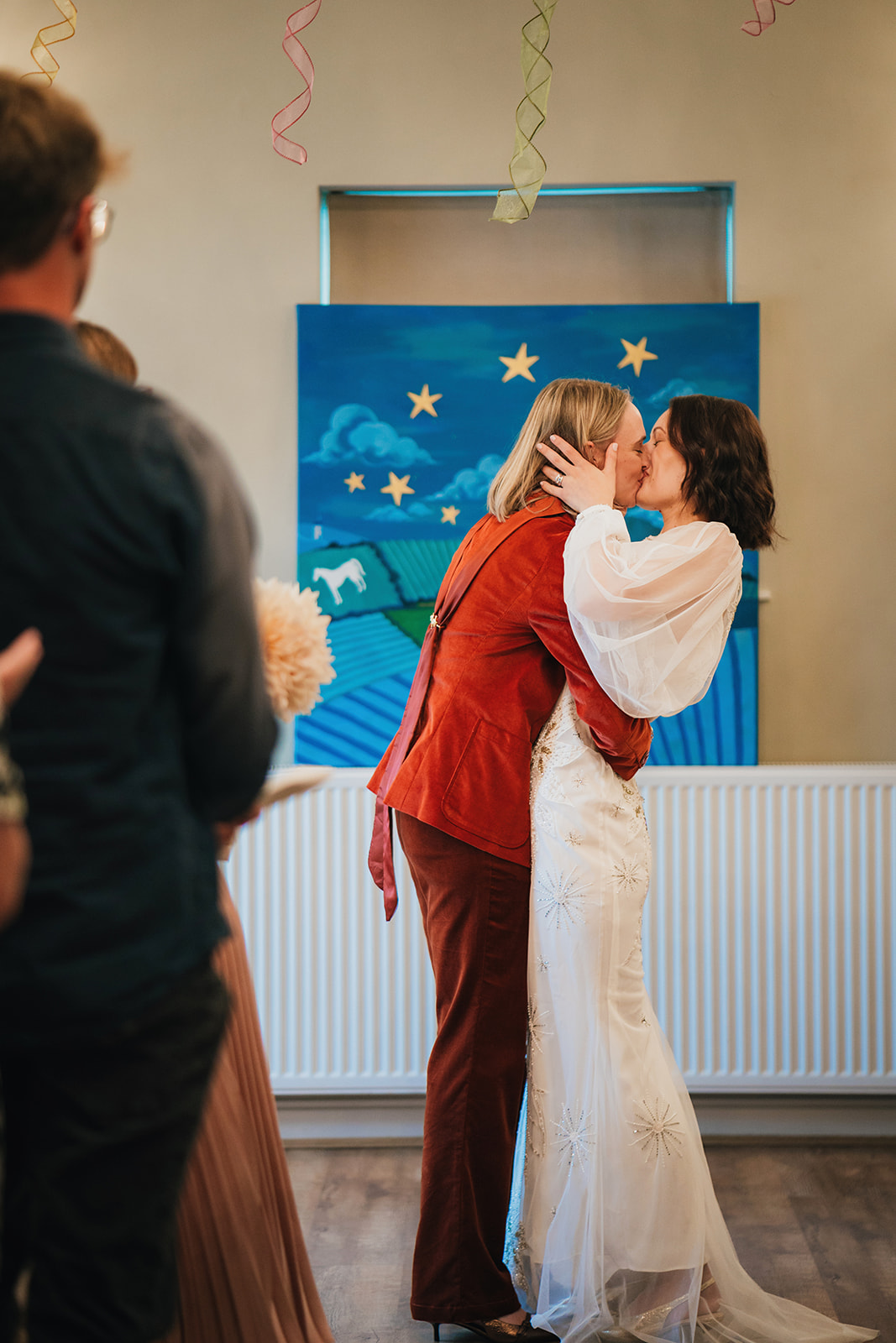 two brides kiss in front of a hand painted picture which creates the ceremony backdrop