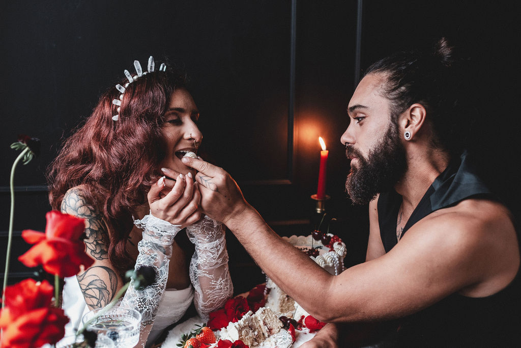 groom feeding his tattooed bride wedding cake in a dark setting